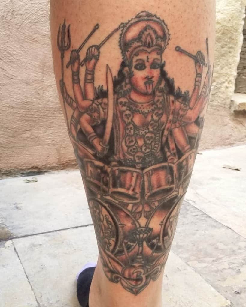 Tattoo of Kali playing drums with multiple arms, holding tridents and swords, adorned with skulls