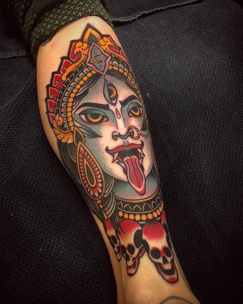 Colorful tattoo of Kali with a third eye, tongue out, adorned with skulls and intricate details