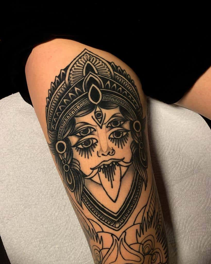 Bold black tattoo of Kali with a third eye, sticking out her tongue, and intricate designs