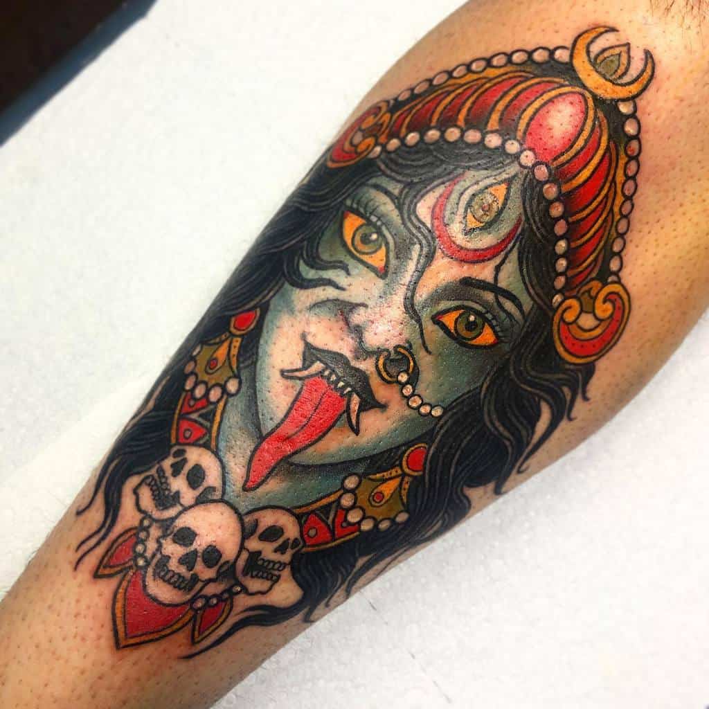 Colorful tattoo of Kali with a third eye, sticking out her tongue, wearing a red crown, adorned with skulls