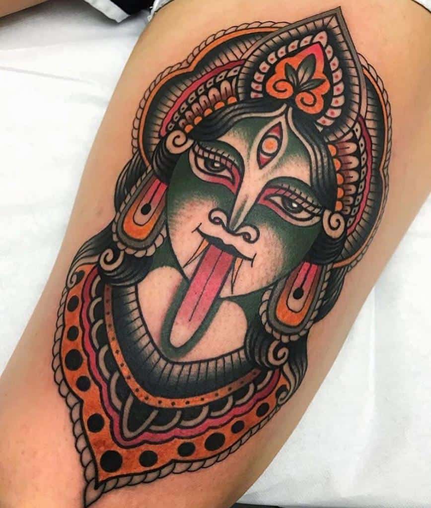Colorful tattoo of Kali with a third eye, sticking out her tongue, adorned with intricate patterns and a detailed headdress