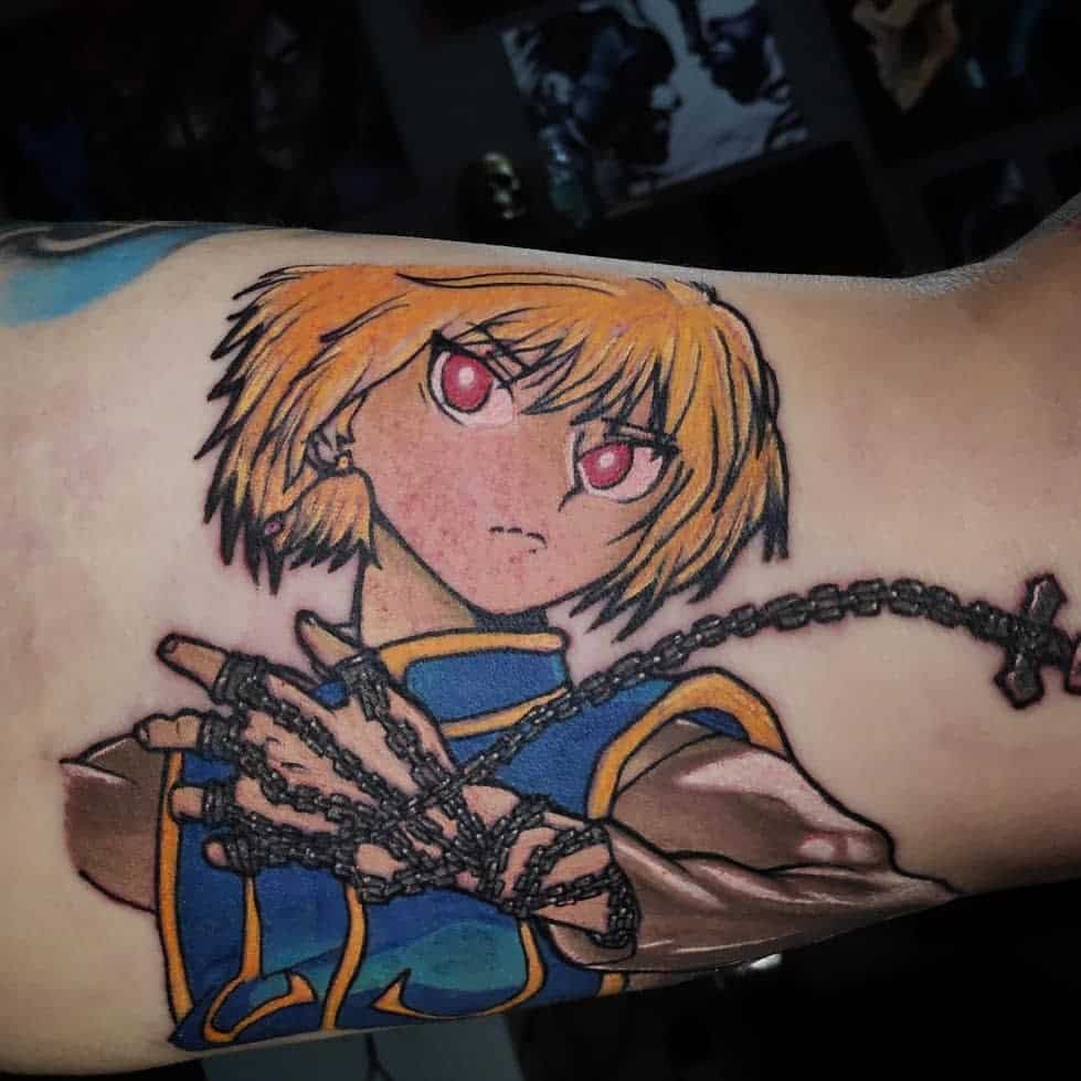 Vibrant Kurapika tattoo from Hunter X Hunter, showcasing his determined expression with red eyes, and intricate chains wrapped around his hand