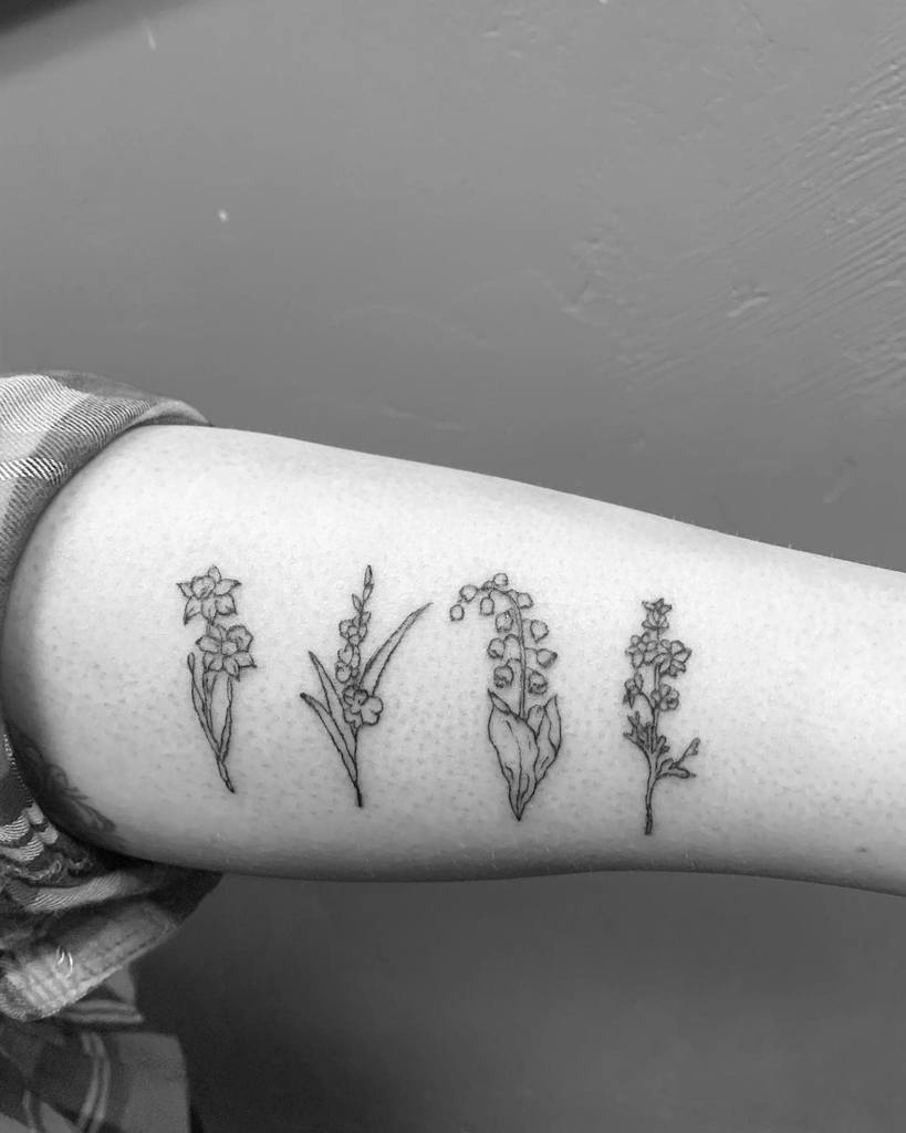 Four different small flower tattoos on a forearm in black ink