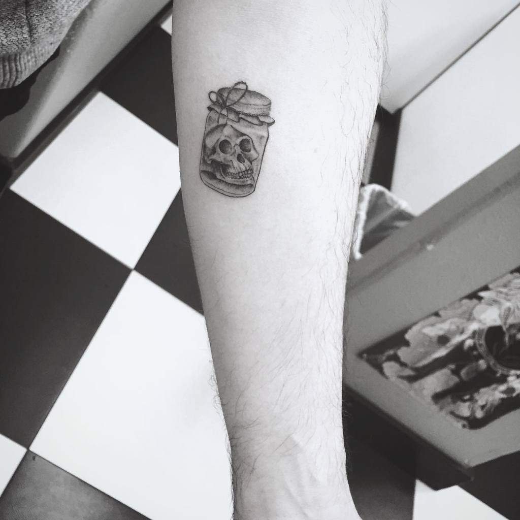Tattoo of a skull in a jar located on the forearm of a person, expertly crafted with single needle precision