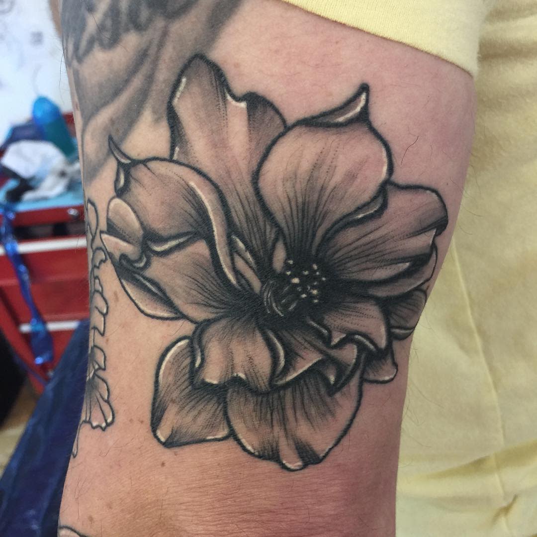 Tattoo of a large, detailed larkspur flower in black ink on an arm