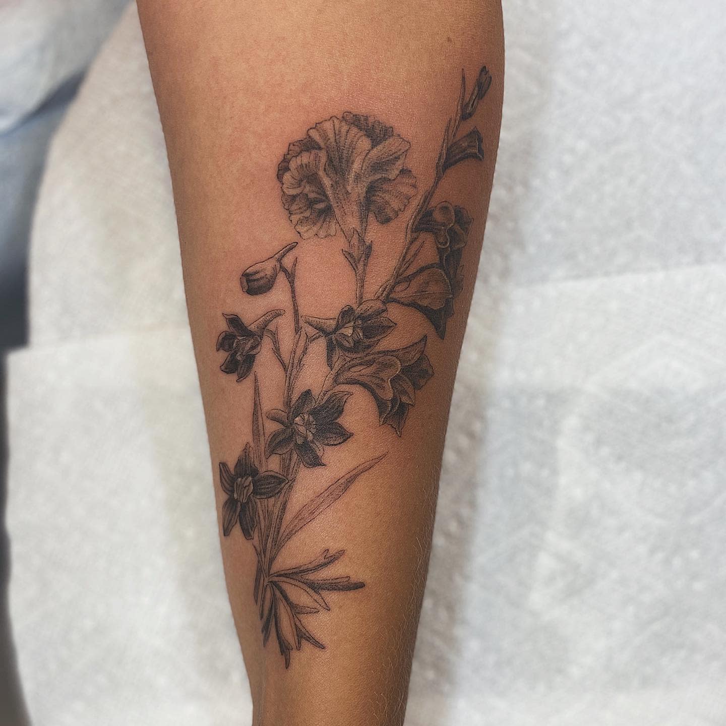Forearm tattoo with detailed, realistic black and grey flowers and leaves