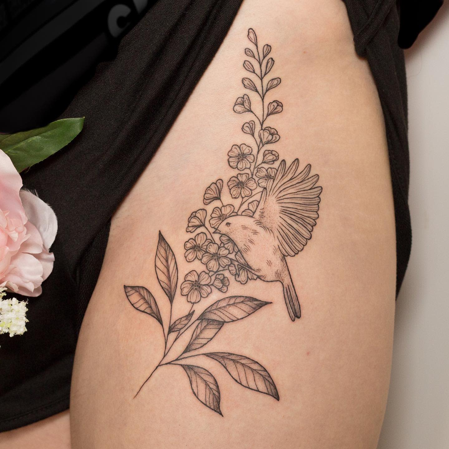 Tattoo of a bird with larkspur flowers and leaves on an upper arm