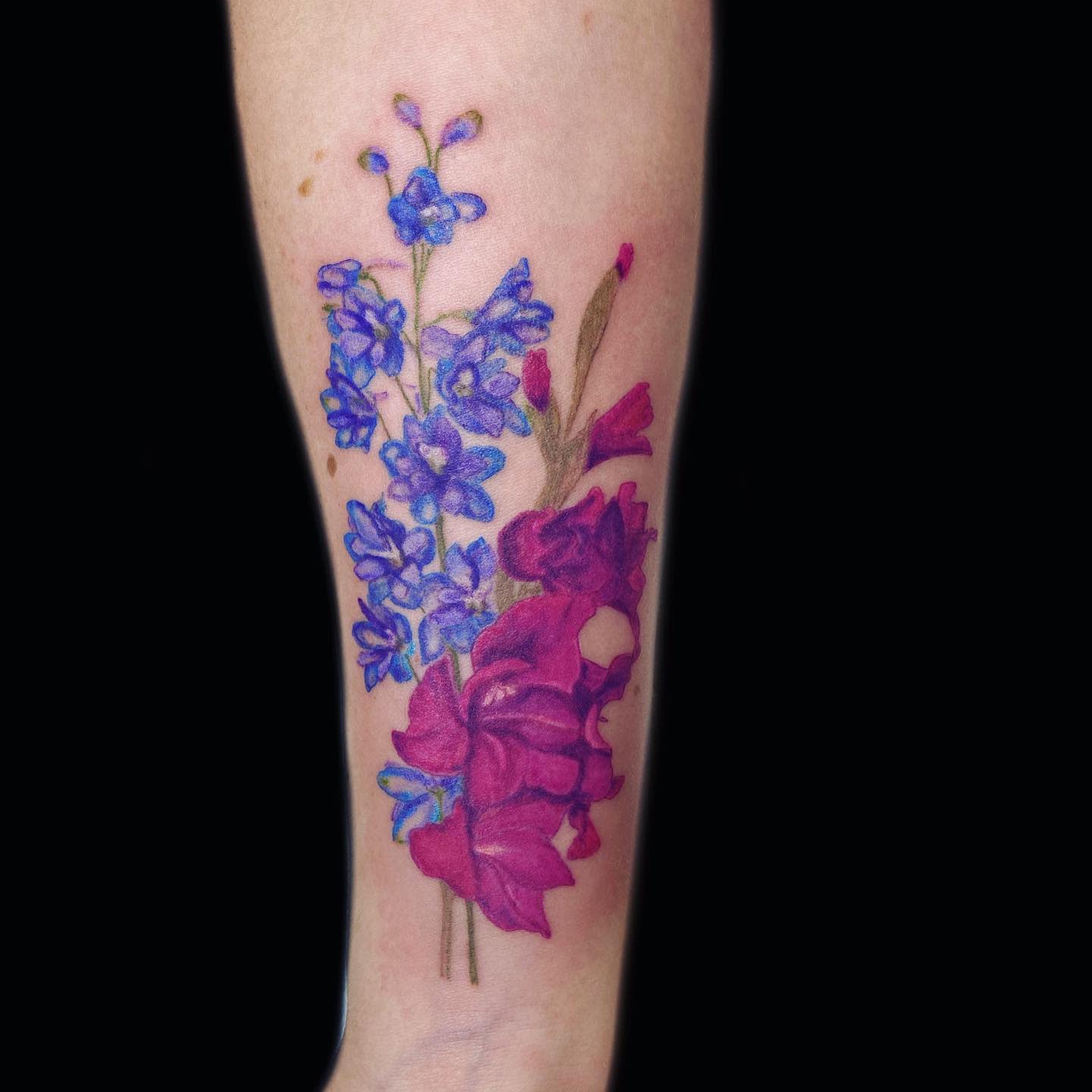 Tattoo of purple larkspur and pink flowers on a forearm