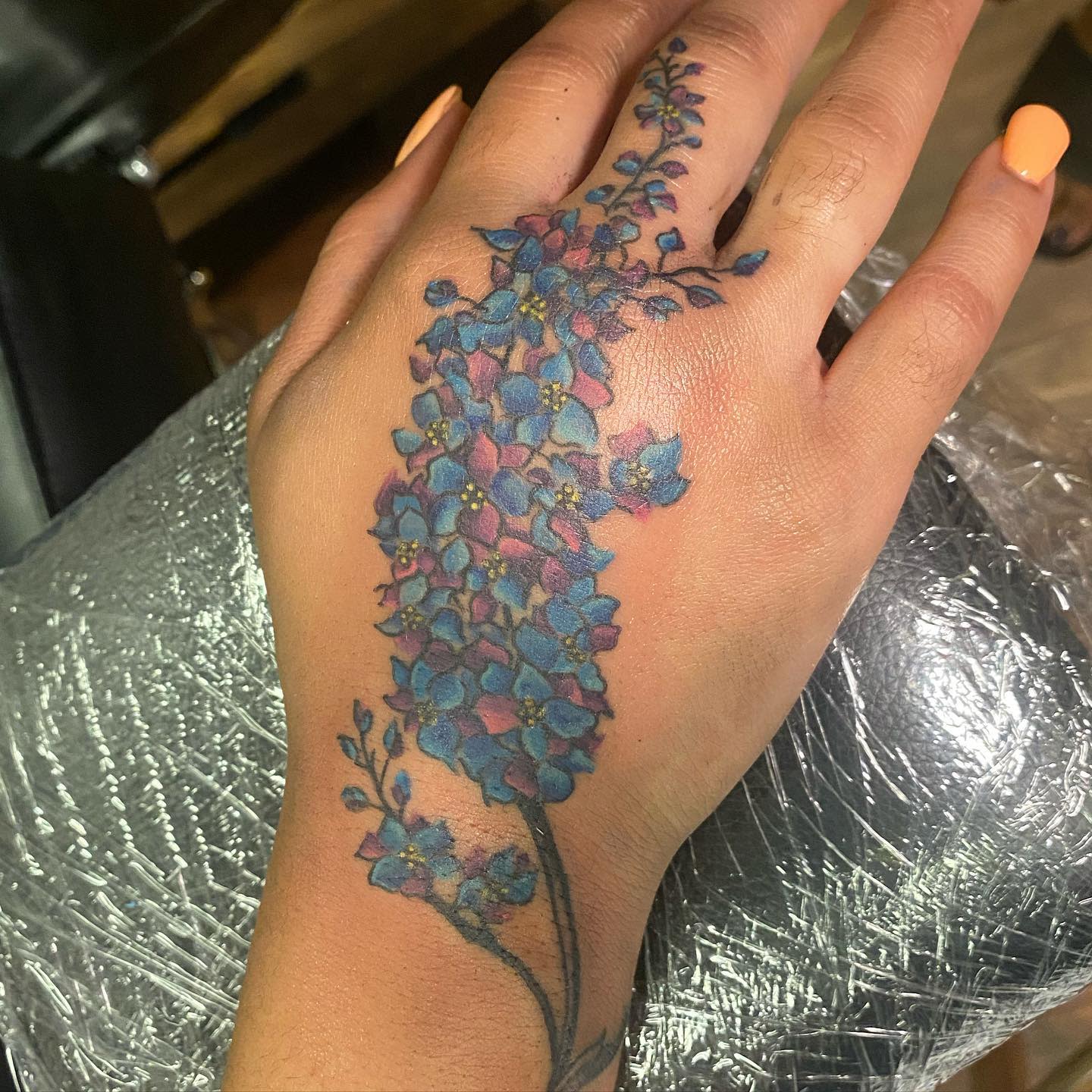 Hand with a blue and purple floral tattoo, delicate flowers extending from wrist to fingers