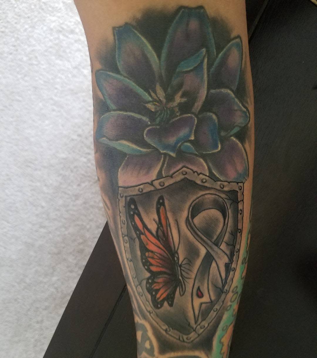 Tattoo of a flower above a shield with a butterfly and an awareness ribbon inside