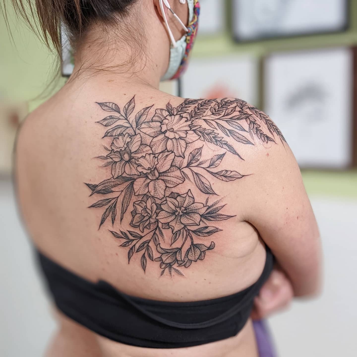 A woman with a large larkspur floral tattoo on her back shoulder