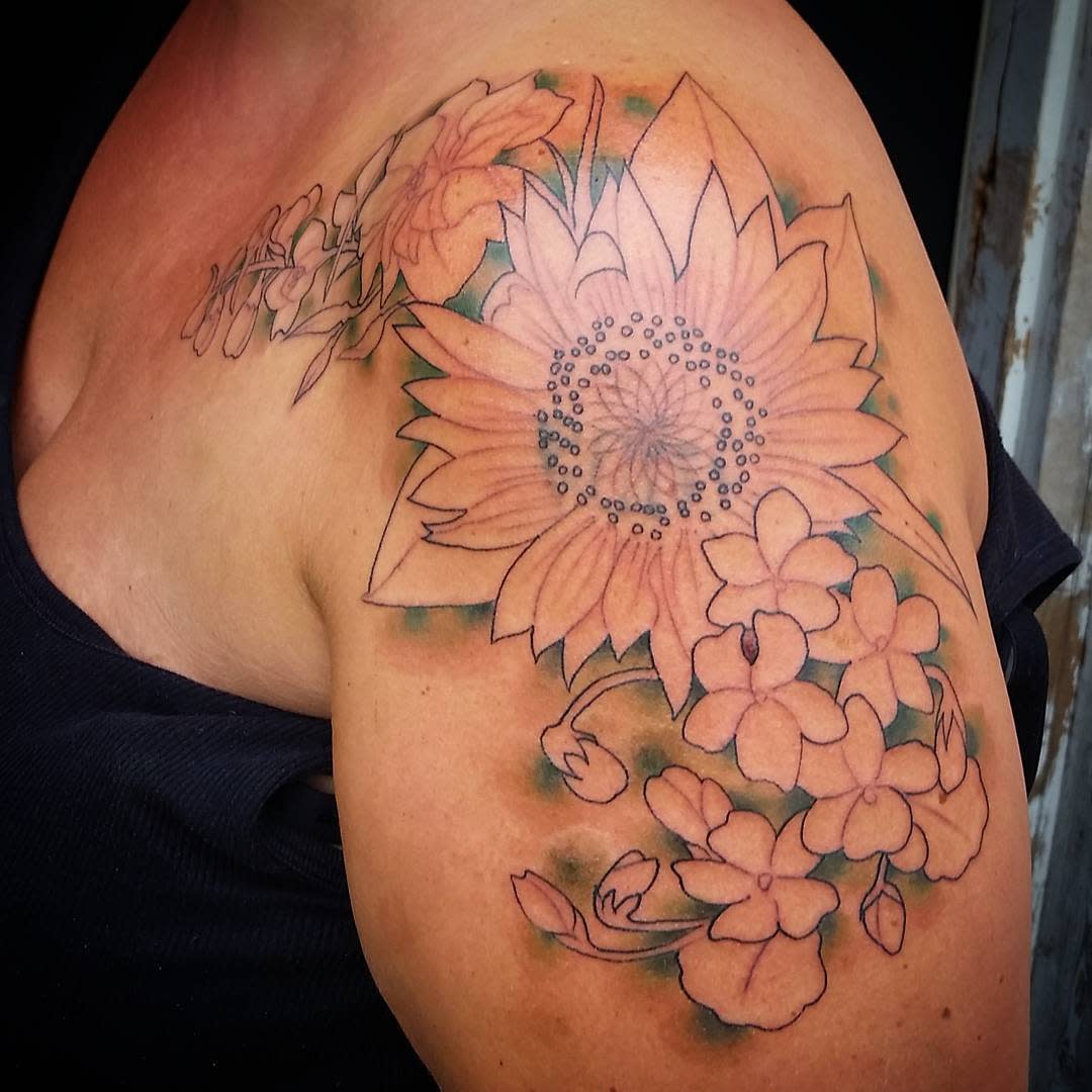 Shoulder tattoo of a sunflower and other flowers, partially colored, on an upper arm