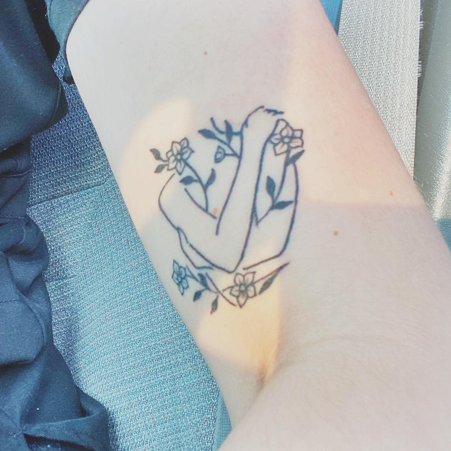 Tattoo of two intertwined arms surrounded by larkspur flowers on an inner arm