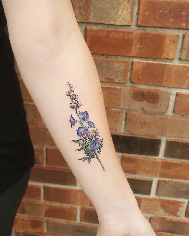 Forearm with a tattoo of larkspur purple flowers and green leaves