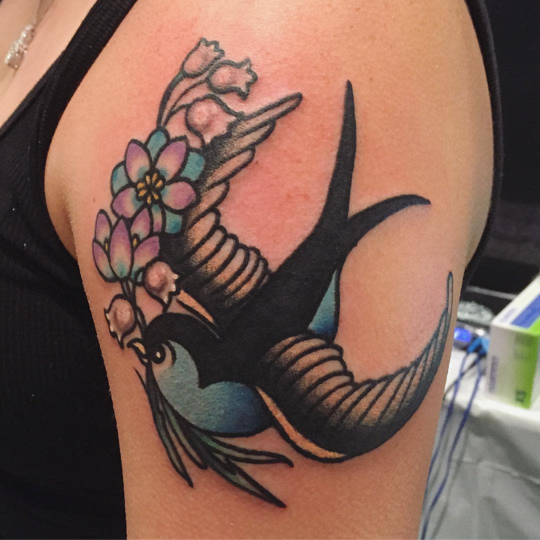Colorful tattoo of a flying bird with purple flowers on an upper arm
