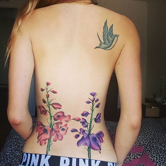 Woman showing a colorful flower tattoo on her lower back and a detailed bird tattoo on her upper back