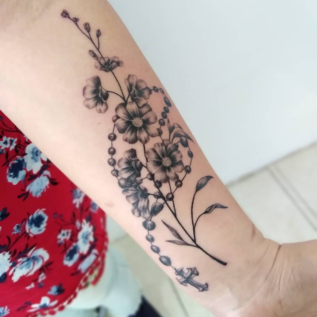 Floral tattoo featuring larkspur flowers and leaves on a forearm