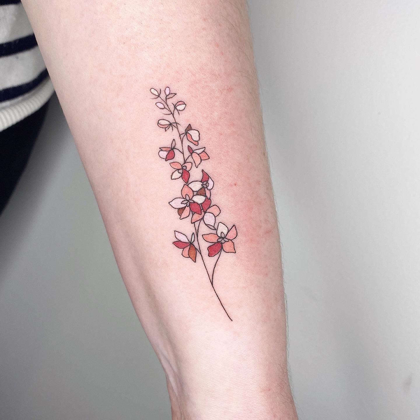 A delicate floral tattoo with pink and red larkspur flowers on a forearm