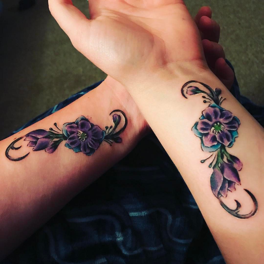 Matching floral tattoos in purple and green ink on the inner forearms