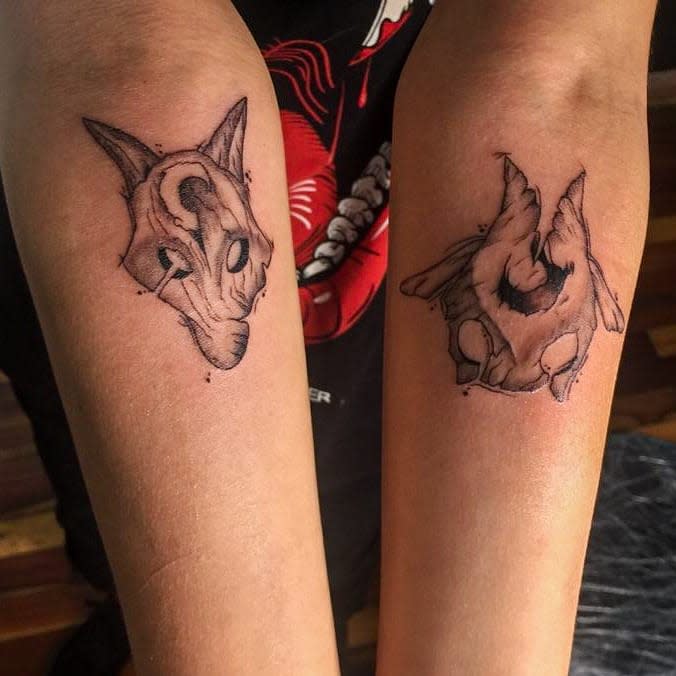 Small, detailed tattoos of Kindred's Wolf and Lamb masks from League of Legends on each forearm