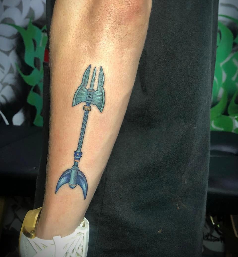 Small tattoo of Pantheon’s spear from League of Legends, rendered in blue tones on the forearm
