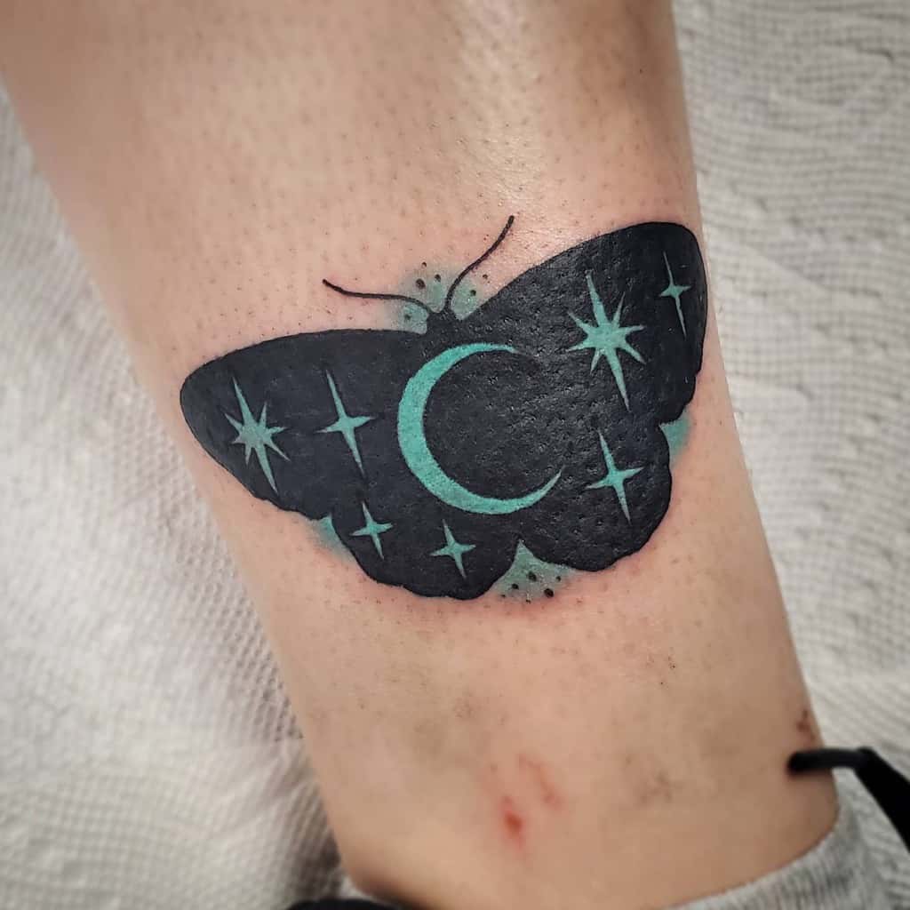 Tattoo of a black butterfly with teal stars and a crescent moon on a person's skin