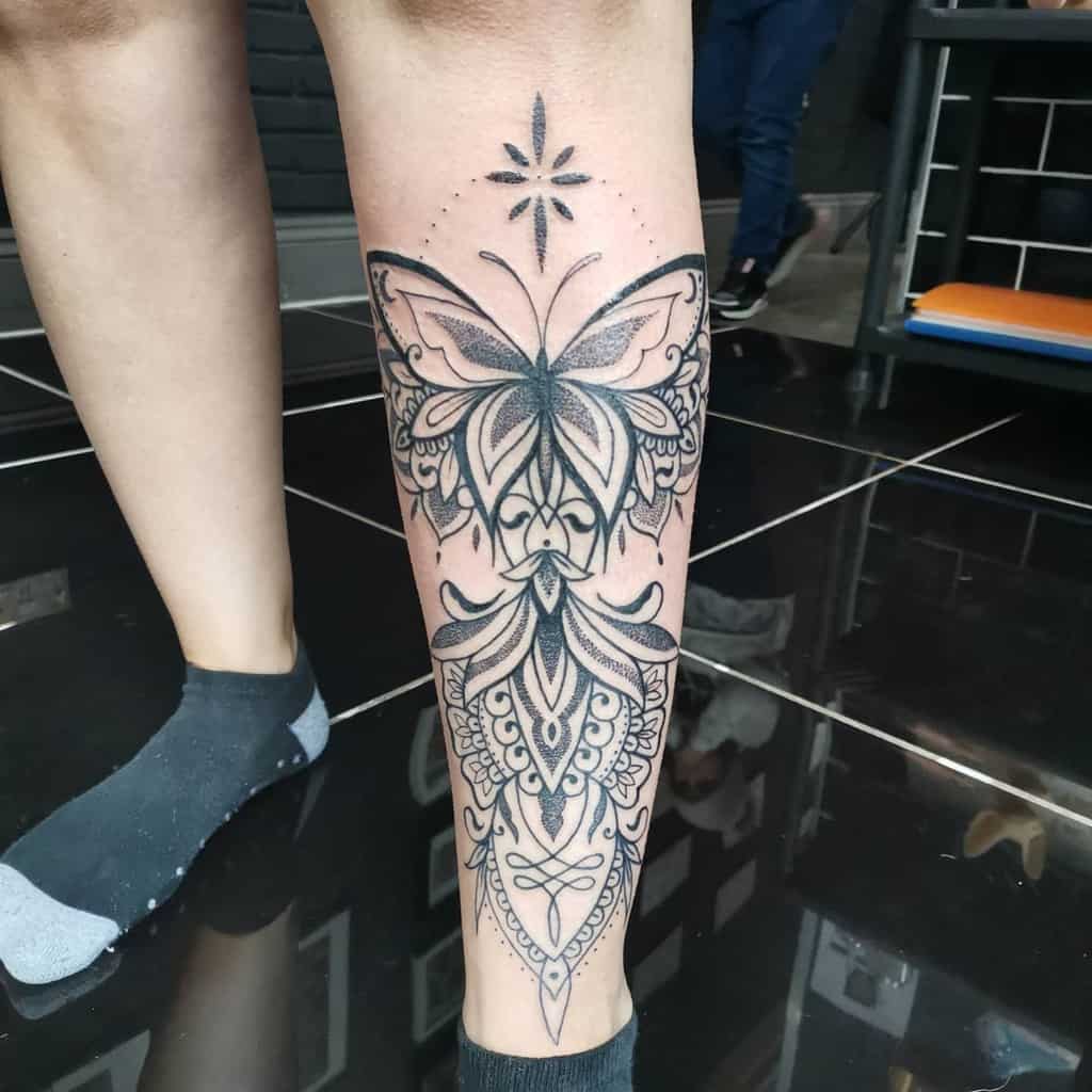 Leg tattoo featuring a detailed butterfly design with symmetrical patterns and a star above
