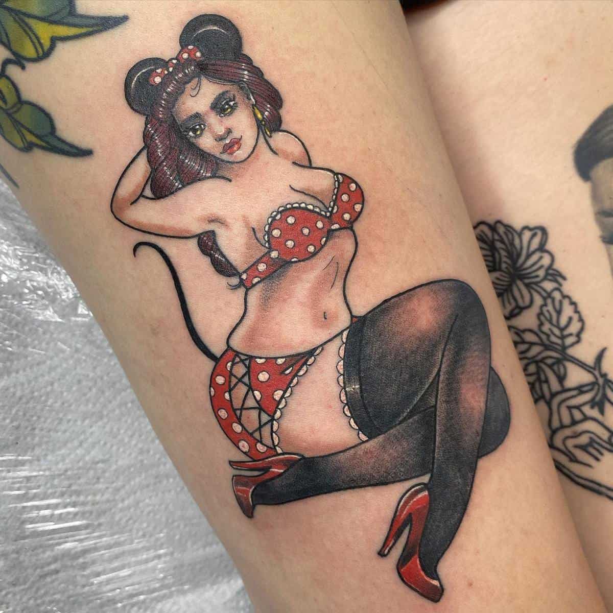 Tattoo of a woman in a polka-dot outfit and mouse ears, striking a pin-up pose on a leg