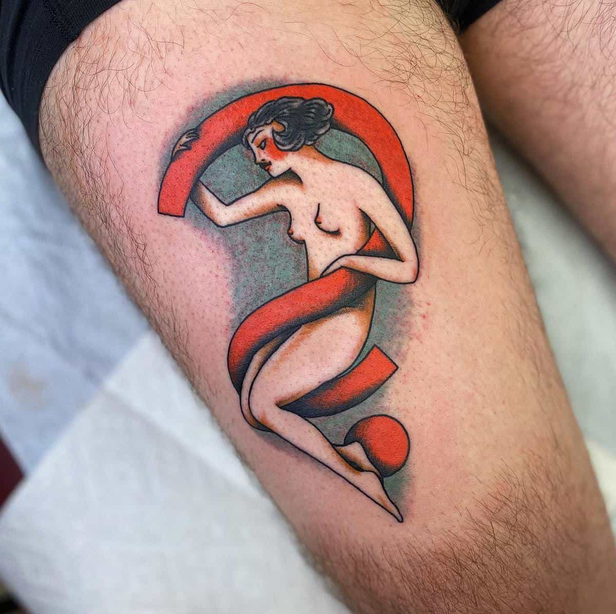 Tattoo of a nude woman wrapped in a red ribbon on a thigh, with the ribbon forming a question mark