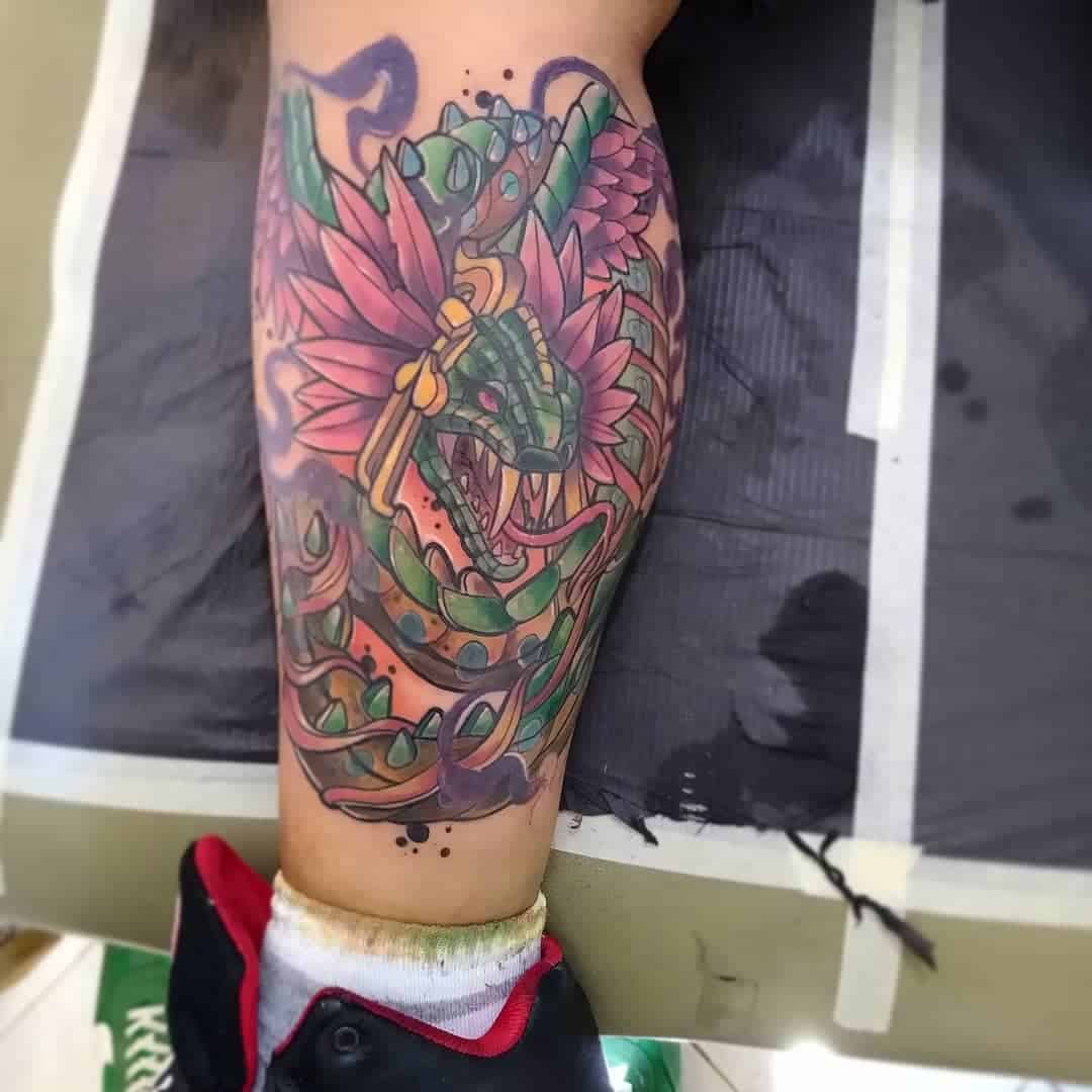 Colorful Quetzalcoatl leg tattoo featuring a vibrant feathered serpent with intricate green scales and pink feathers