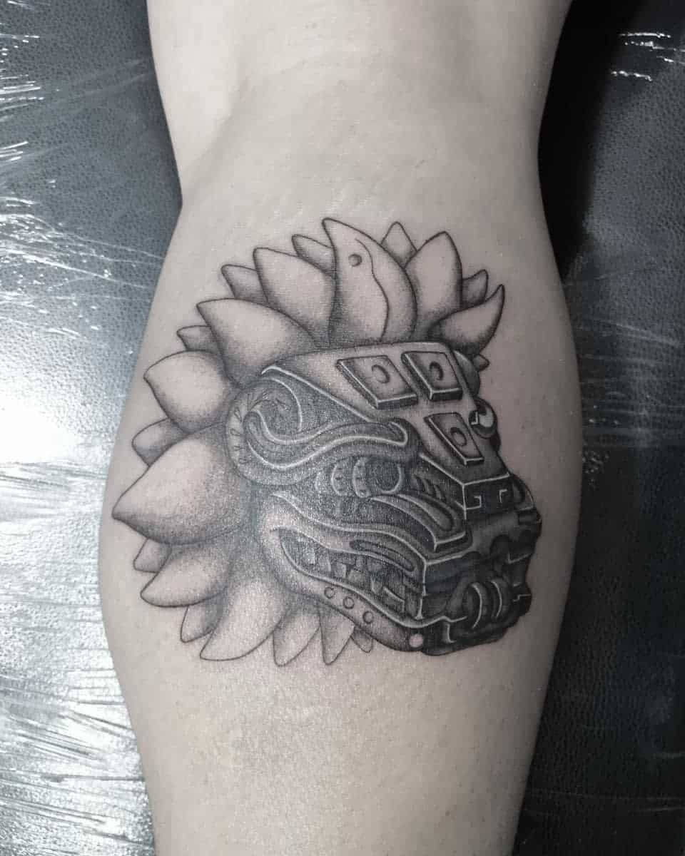 Black and gray Quetzalcoatl leg tattoo featuring a detailed feathered serpent head with bold shading