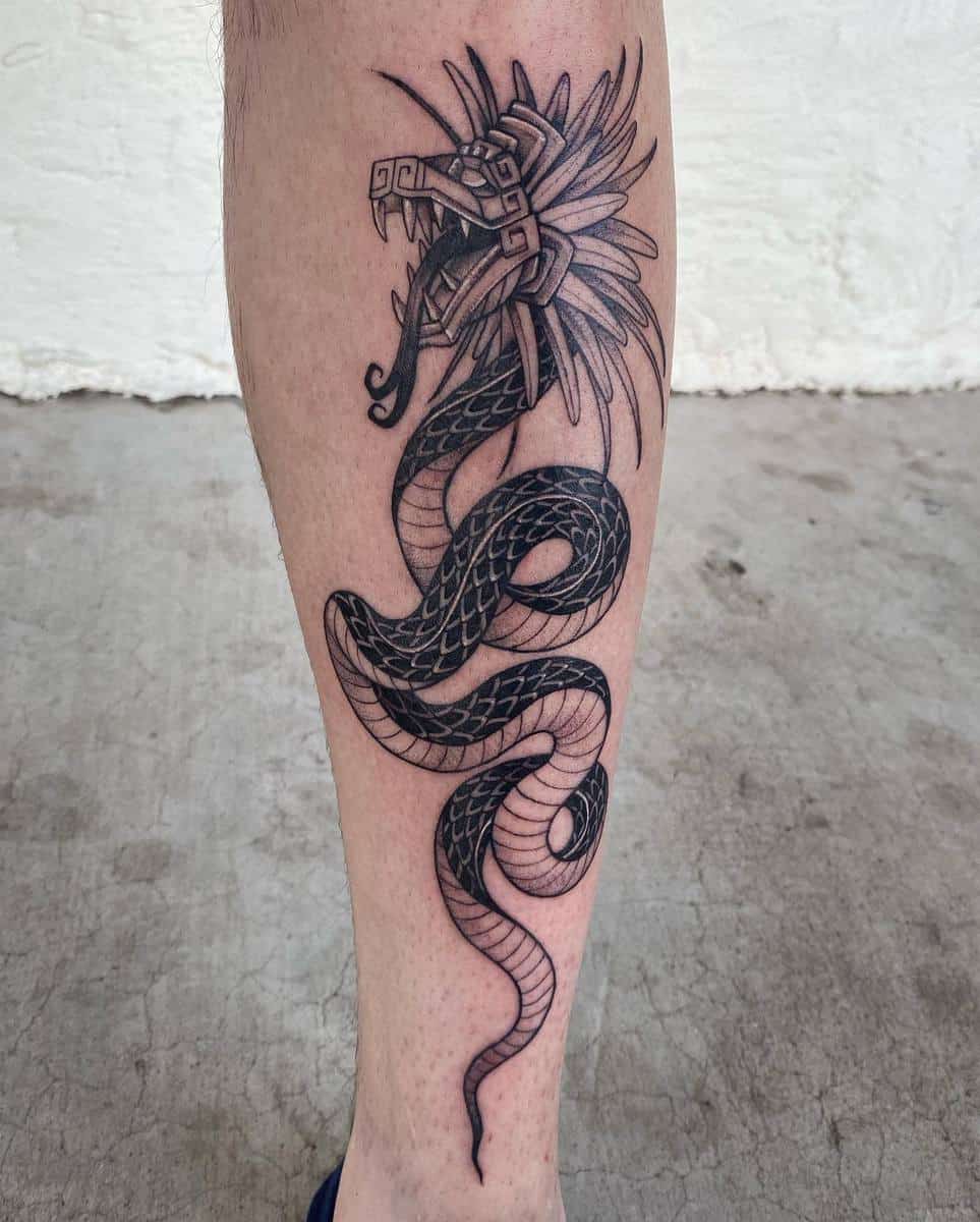 Black and gray Quetzalcoatl leg tattoo featuring a coiled serpent body with a detailed feathered head
