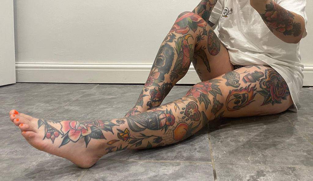 This vibrant leg sleeve tattoo is a masterpiece of colorful imagery, featuring bold floral designs, skulls, and intricate traditional motifs that flow seamlessly across the legs for a striking visual impact