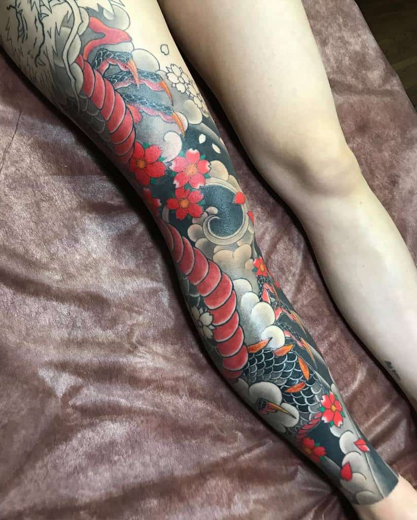 Leg with a colorful koi fish and cherry blossom tattoo on a brown surface