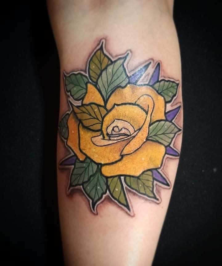 Tattoo of a yellow rose with green leaves and a purple background on an arm