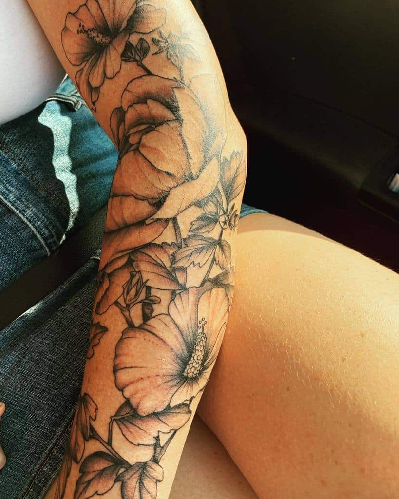A sleeve of large floral tattoos, showcasing hibiscus flowers in black ink, adorns the arm