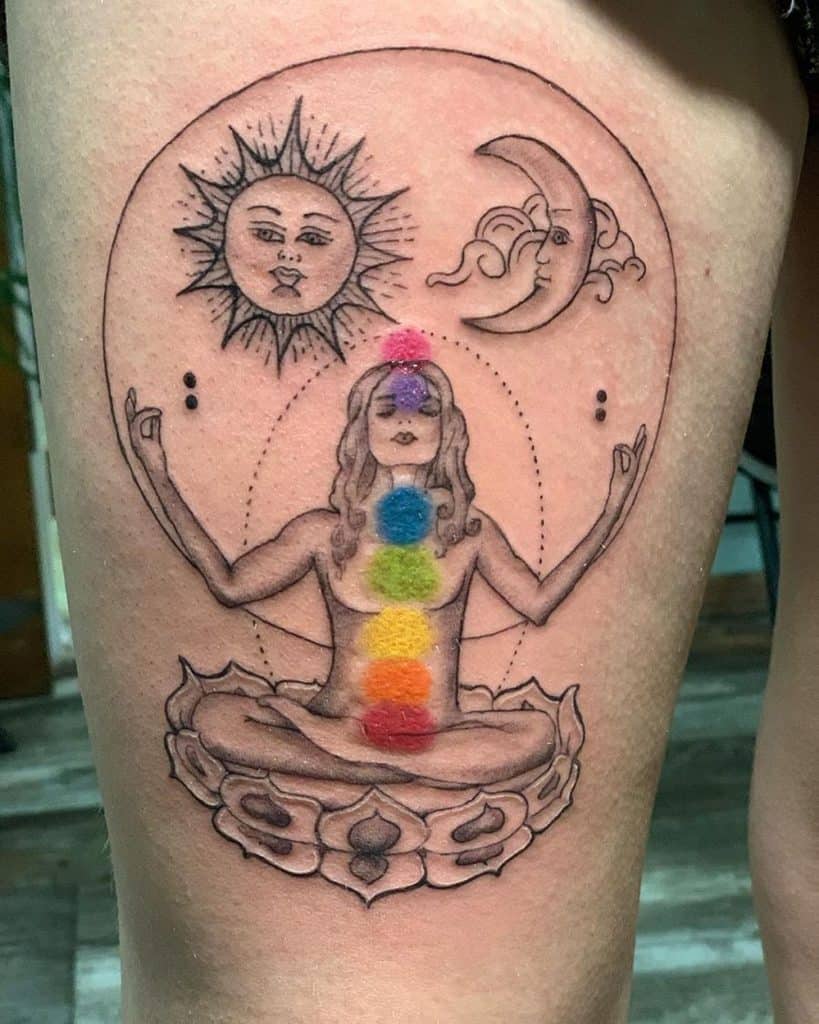 Black ink tattoo of a meditating woman with colored chakras, a sun and moon above, and intricate spiritual symbols.