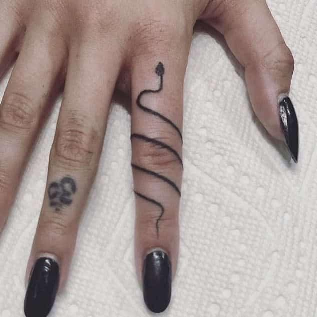A black ink ring tattoo of a winding snake coiling around the finger, ending in a pointed head, resembling a serpent's shape