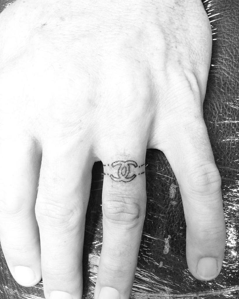 A minimalist ring tattoo of the Chanel logo, with two interlocking C's, surrounded by two dotted lines