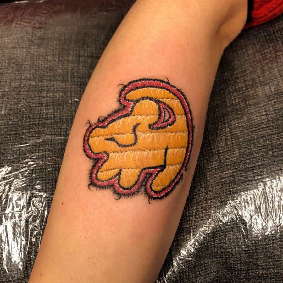 Stylized embroidered tattoo of a lion emblem, with bold stitch-like details and a vibrant, handcrafted textile effect.