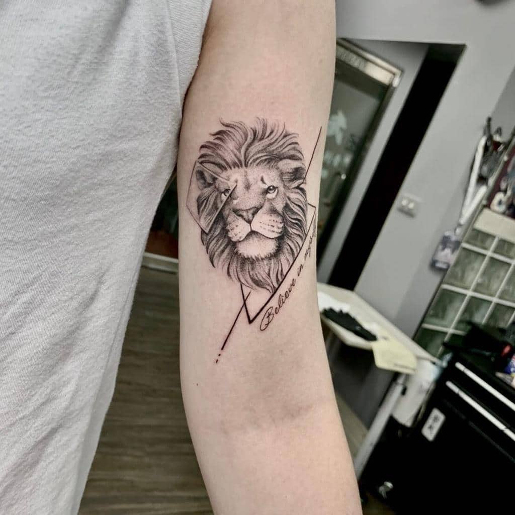 Arm tattoo of a lion with text "Believe" and geometric lines