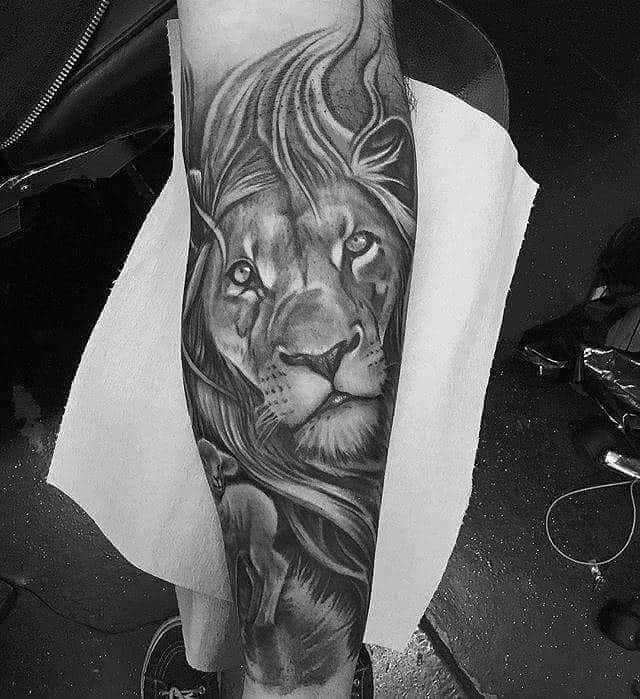 Black and white tattoo on an arm, featuring a lion with detailed shading and a long mane