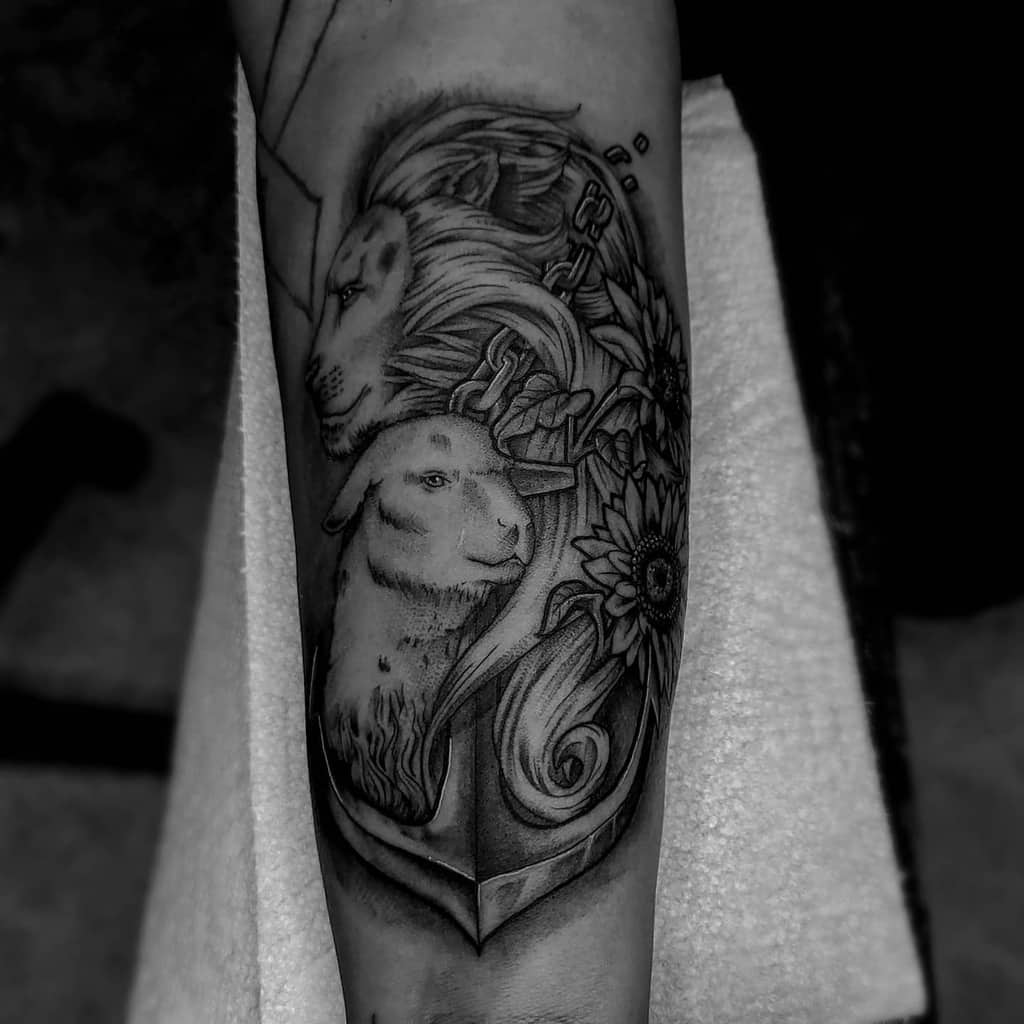 Tattoo of a lion and a lamb with flowers on an arm, intricately done in black and grey ink
