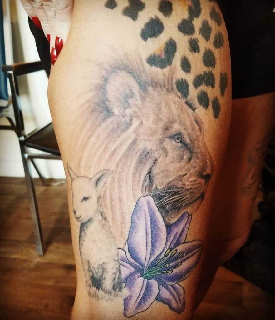 Tattoo featuring a majestic lion, gentle lamb, delicate lily, and striking leopard spots on a person's thigh