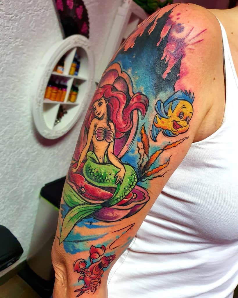 A vibrant sleeve tattoo of Ariel with Flounder and Sebastian, surrounded by ocean elements, a shell, and colorful underwater scenery