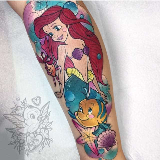 A playful tattoo of Ariel with Sebastian and Flounder, surrounded by bubbles, a starfish, and seashells in a vibrant underwater scene