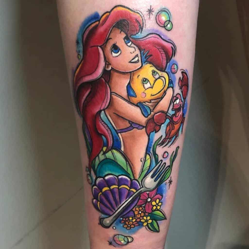 A colorful tattoo of Ariel holding Flounder with Sebastian nearby, surrounded by bubbles, seashells, flowers, and a fork in a vibrant design