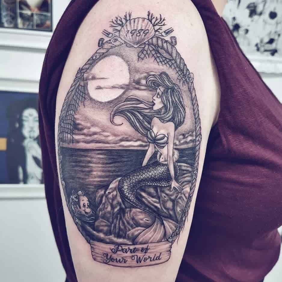 Black-and-white tattoo of Ariel sitting on a rock under a moonlit sky, framed by nautical rope and the text 'Part of Your World'