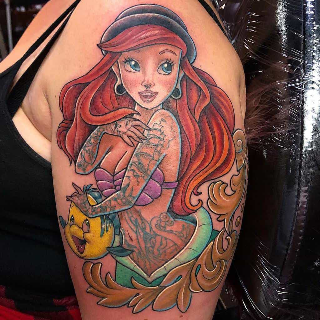 Colorful tattoo of the Little Mermaid with vibrant red hair, Flounder, and intricate undersea details on an upper arm