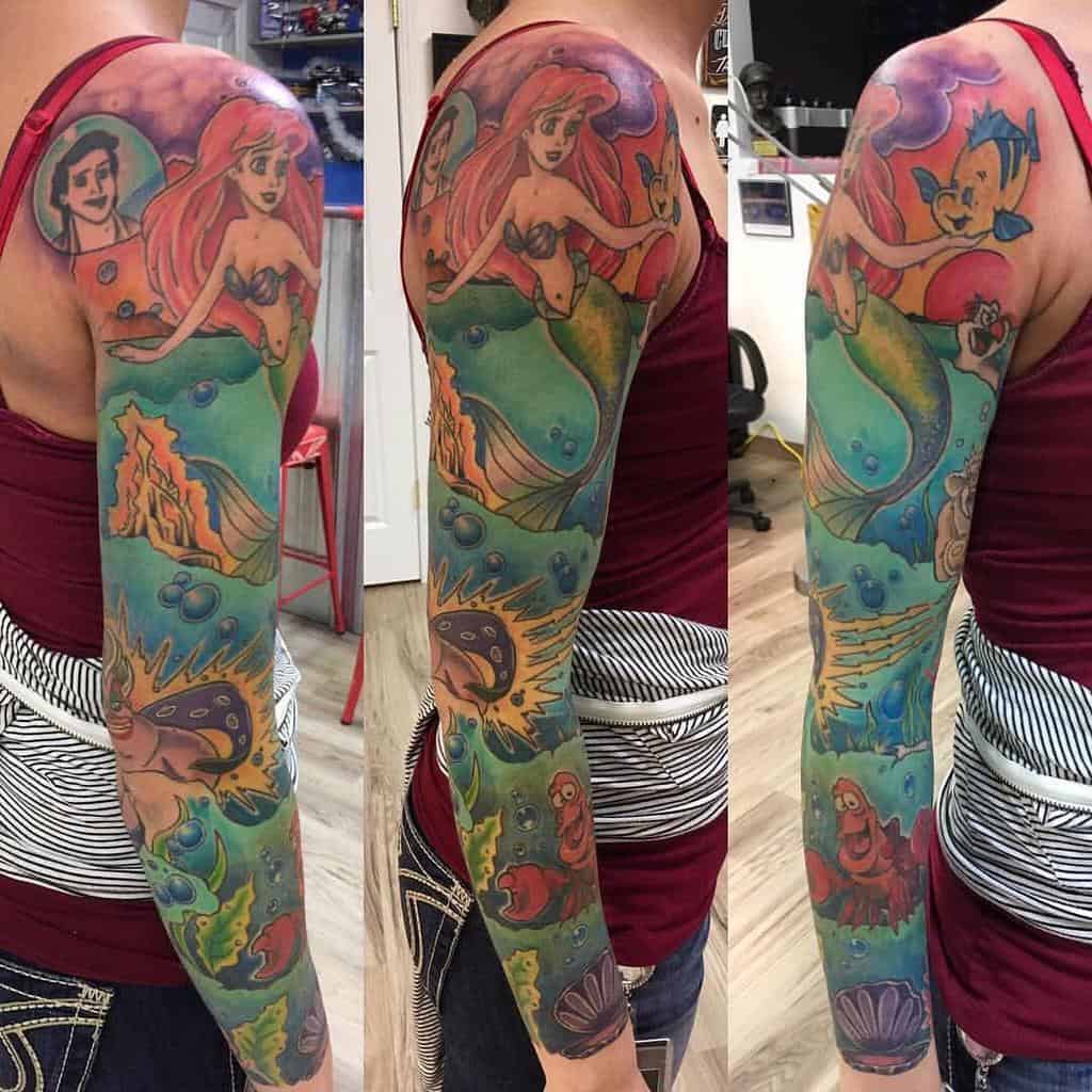 Detailed full sleeve tattoo featuring Ariel, Prince Eric, Flounder, Sebastian, and vibrant undersea elements in a colorful underwater scene